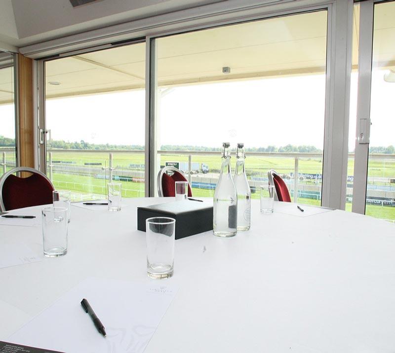 A table neatly prepared with a view of the racecourse available through the windows in the background.