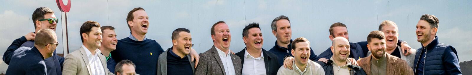 A large group of guys posing in front of the backdrop at Lingfield Races