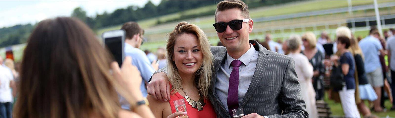 Couple posing for a photo at the races with the crowds in the background.