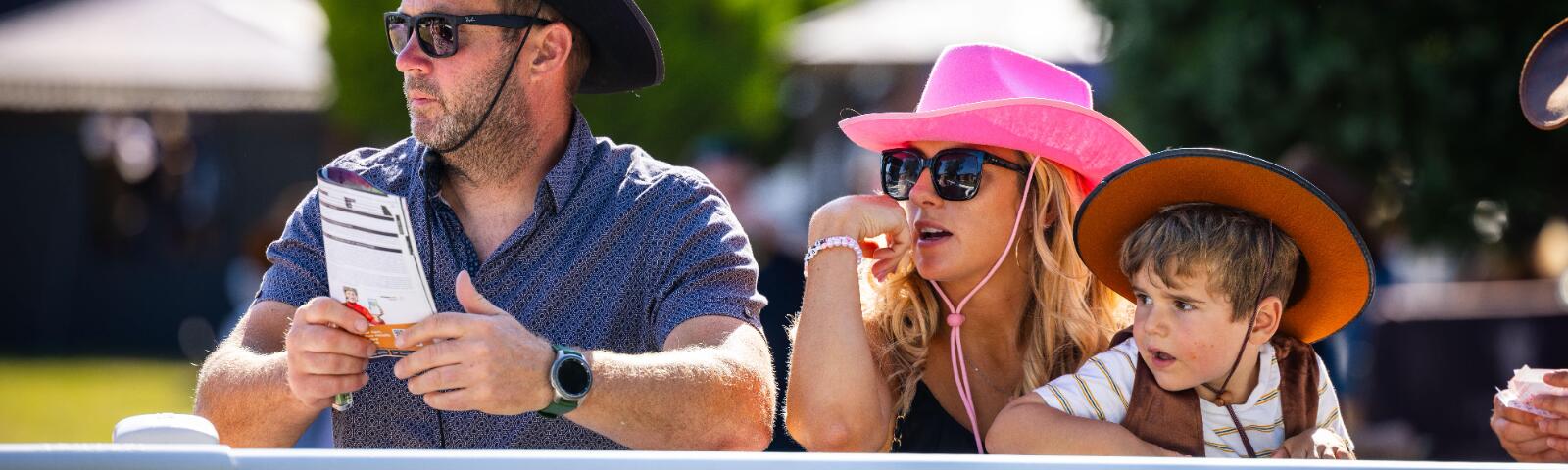 A family at Lingfield Races watches the parade ring, with one holding a race card