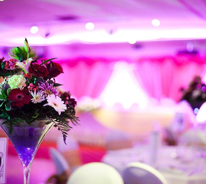 Close up on a glass vase with flowers, standing on a table, in a room dressed up for a wedding.